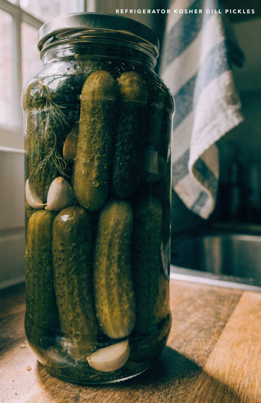 Jar of refrigerator kosher dill pickles spears in a glass jar with fresh dill on a wooden counter